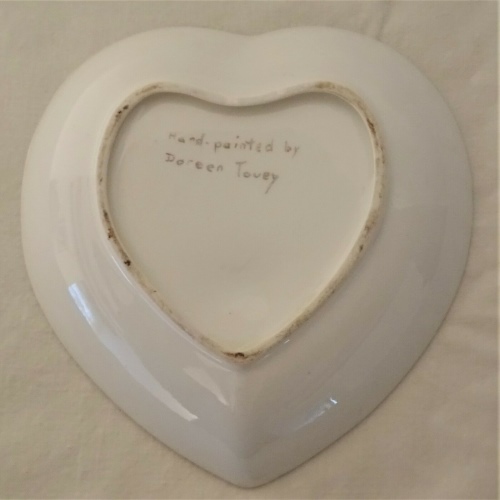 White underside of heart-shaped dish marked as 'Hand-painted by Doreen Tovey'.