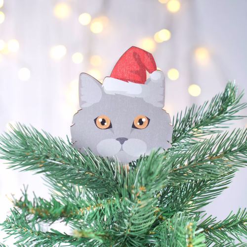 Tree topper of a gray cat with orange eyes wearing a Santa hat, at the top of a Christmas tree