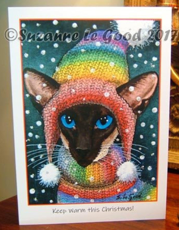 Siamese cat in snowstorm wearing rainbow knitted bobble hat. Christmas card by Suzanne Le Good.