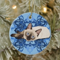 Chocolate point Siamese kitten on a blue floral background; circular tree decoration with gold hanging cord