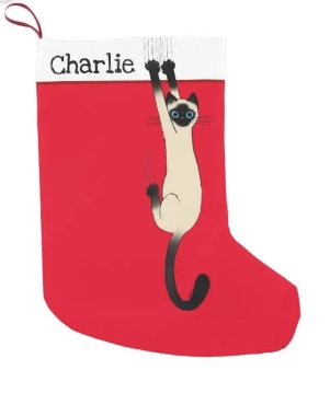 Red and white Christmas stocking featuring Siamese cat hanging off wall